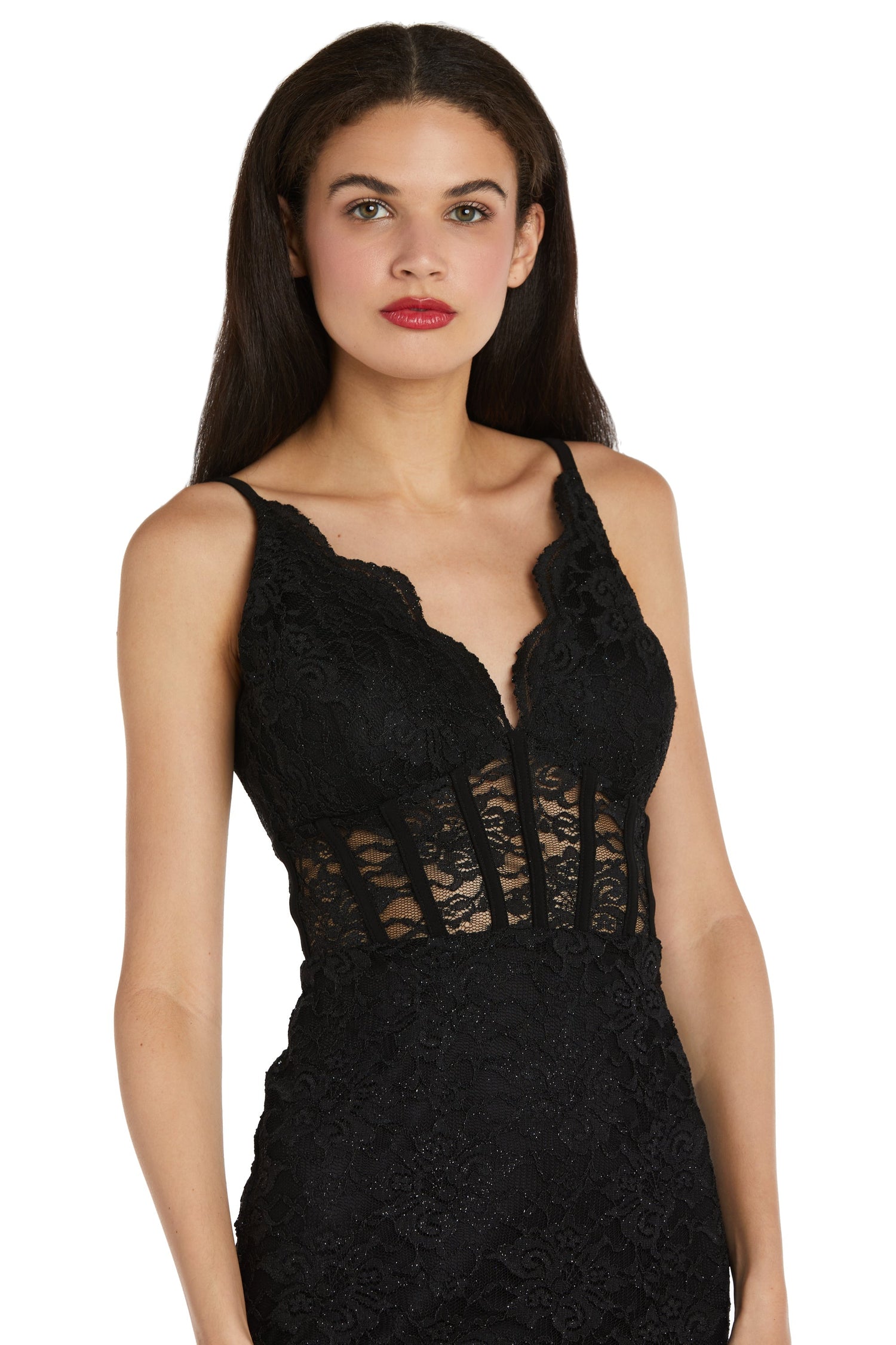A woman wears the Morgan 12976 short lace party dress, featuring a sleeveless black design with a scalloped v-neckline and sheer lace corset bodice panels, looking forward.
