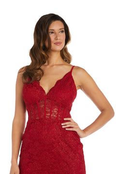 Woman in the Morgan 12976 Short Lace Party Dress—sleeveless, red with deep V-neckline, corset bodice, and sheer panels—stands with one hand on her hip against a white background.