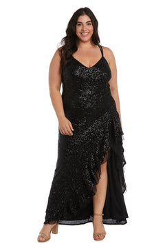 A woman stands smiling in beige open-toe heels, wearing the Morgan 13029WM—a long black plus-size sequin prom dress featuring a v-neckline, ruffled skirt, and a slit.