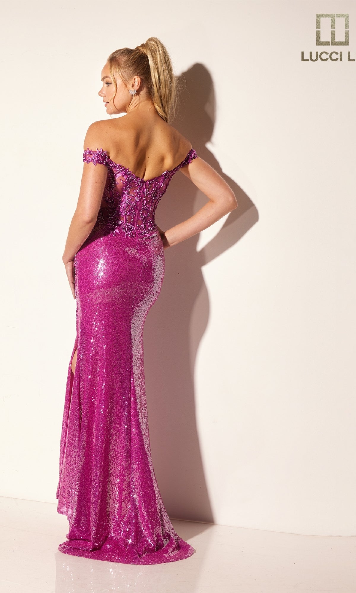 A woman models the Lucci Lu 1308, an off-the-shoulder, floor-length pink sequin prom dress with a slit, set against a plain background.