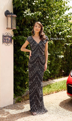 A woman wearing the Primavera 13138 Long Formal Dress stands outside near a wall lantern and red car, with greenery in the background. "PRIMAVERA" is displayed nearby.
