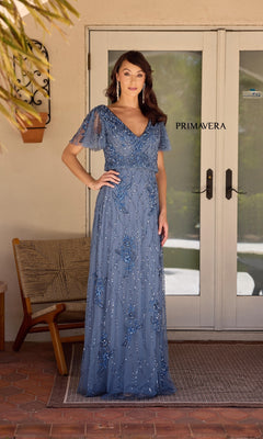 A woman stands outside a glass door wearing the Long Formal Dress: Primavera 13144—a floor-length, short-sleeved blue gown adorned with elegant beadwork.