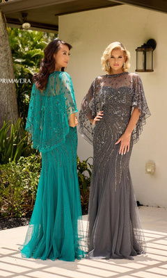 Two women stand outdoors in long beaded formal dresses—one wears the Sheer Capelet Long Formal Dress: Primavera 13145 in teal with a removable capelet, and the other wears a gray dress—posing before a light-colored building.