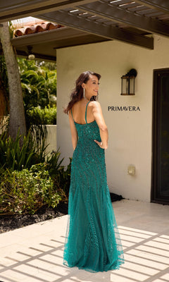 A woman stands outdoors, facing away from the camera near a beige building marked "PRIMAVERA," wearing the Sheer Capelet Long Formal Dress: Primavera 13145 with a mermaid skirt.
