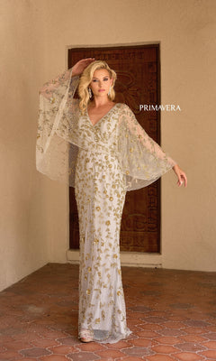 A woman stands before a wooden door wearing the Primavera 13149 long formal dress, featuring gold beading, sheer wide sleeves, and a v-neckline. The word "PRIMAVERA" appears beside her.