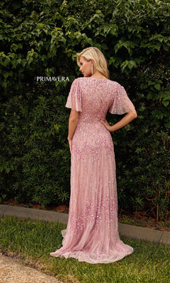 A woman stands outdoors with her back to the camera, wearing the pink Primavera 13153 long formal A-line sequin dress with flutter sleeves. Green foliage is in the background, and "PRIMAVERA" appears on the left.