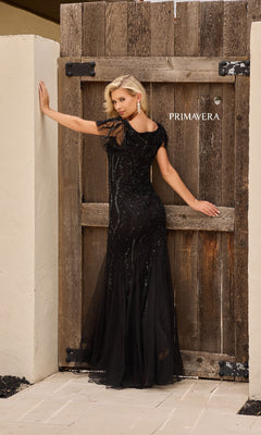 A woman poses by a wooden gate labeled “PRIMAVERA,” wearing the Long Formal Dress: Primavera 13155—a black, floor-length gown with elegant sequin-inspired embellishments, reminiscent of a mermaid dress.