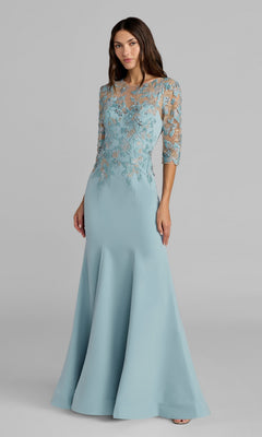 A woman stands against a plain gray background wearing the Mac Duggal 13204 long formal dress in French Blue, featuring sheer, embroidered sleeves and a fitted bodice adorned with delicate floral embroidery.