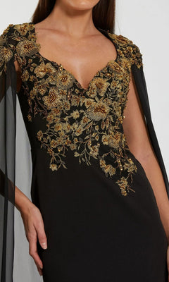 A woman wears the Mac Duggal 13206 long formal dress, featuring sheer black sleeves and intricate gold floral embroidery on the bodice, evoking a sense of timeless elegance.