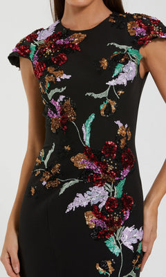 A woman wearing the Mac Duggal 13211 long formal dress, a fitted black crepe trumpet gown featuring vibrant floral sequin embroidery on the bodice and sleeves.