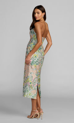 A woman wearing the Mac Duggal 13223 tea-length party dress, featuring a strapless design and delicate floral brocade pattern, stands in profile against a plain gray background, styled with strappy high heels and earrings.