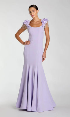 A woman models the Mac Duggal 13232 Long Formal Dress in lilac—a floor-length, fitted gown featuring floral and beaded shoulder embellishments and a graceful mermaid silhouette—posed against a plain light gray background.