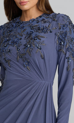 A woman wearing the Mac Duggal 13246 long formal dress, featuring long sleeves, a deep blue hue, and detailed floral applique with beaded embellishments adorning the shoulder and upper bodice.