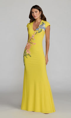 A woman stands against a plain gray background wearing the Mac Duggal 13249 long formal dress in Yellow Multi, a floor-length gown featuring short sleeves and beaded floral appliqué embellishing the upper bodice and hip.