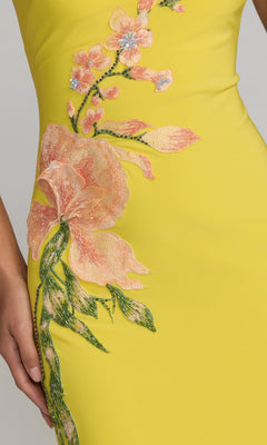 Close-up of the Long Formal Dress: Mac Duggal 13249 in yellow, showcasing pink and green beaded floral applique embroidery, with a hand partially visible on the left side.