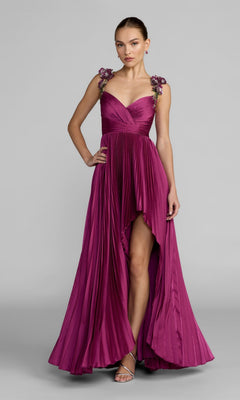 A person wearing the Mac Duggal 13263 long formal dress in magenta, featuring sleeveless styling, a high-low pleated skirt, satin fabric, and intricate 3D floral straps, stands against a plain grey background.