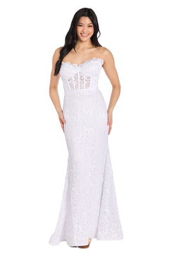 A woman wearing the Strapless Long Lace Prom Dress: Morgan 13269 stands and smiles at the camera; the dress features a fitted bodice, flared mermaid skirt, and elegant white lace design.