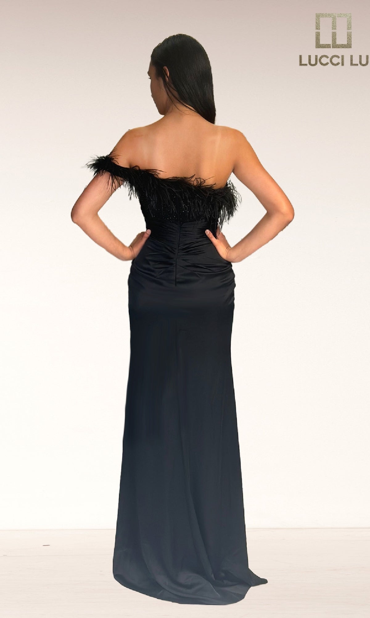 A woman faces away, wearing the Lucci Lu 1326 long black prom dress with feathers and off-the-shoulder details. The 