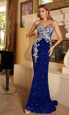 A woman stands indoors wearing the Lucci Lu 1332 Sequin and Velvet Long Prom Dress, a fitted royal blue strapless gown with silver embellishments and a thigh-high slit.