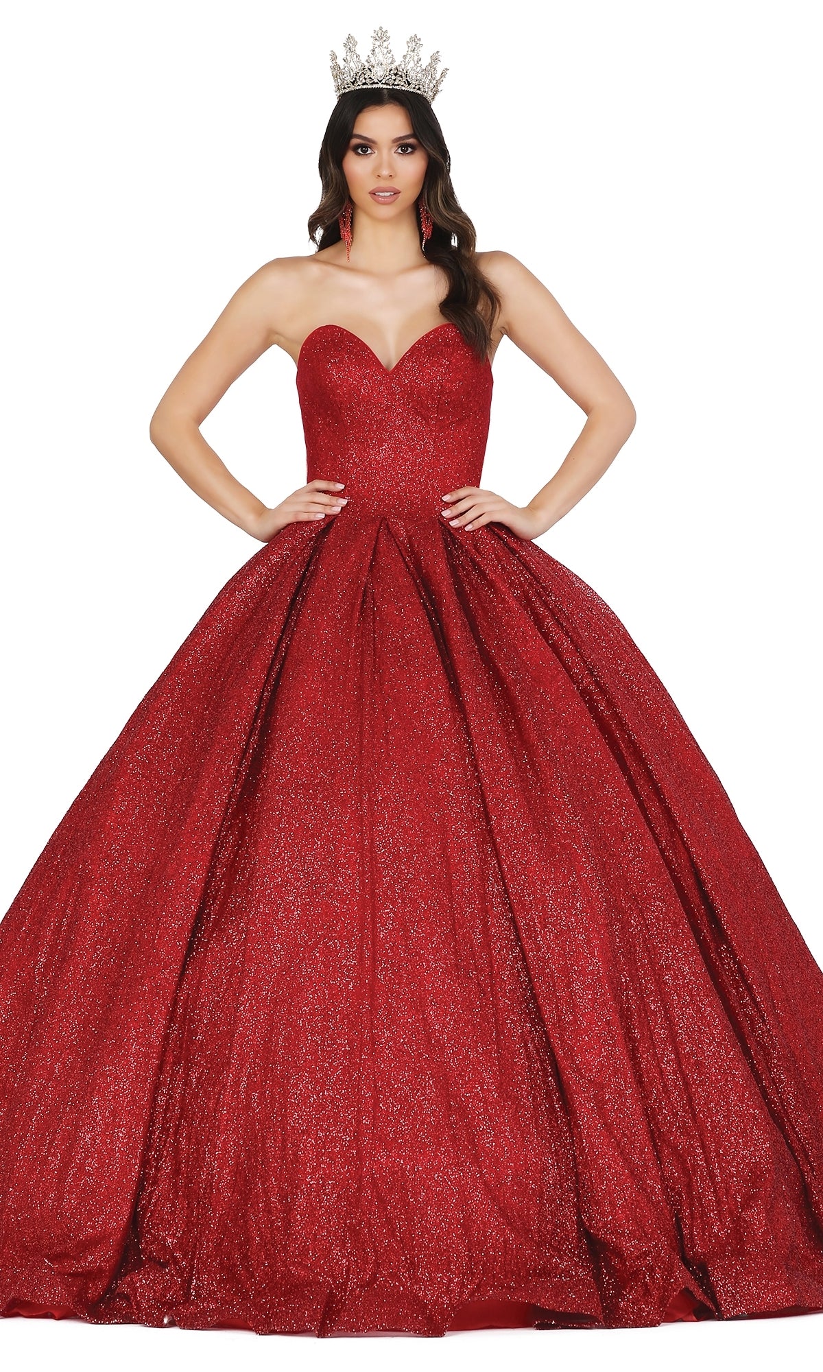 A woman wearing the Quinceanera Dress 1341 by Dancing Queen—a sparkling red ball gown with a strapless sweetheart neckline and a silver crown—stands with her hands on her hips against a white background.