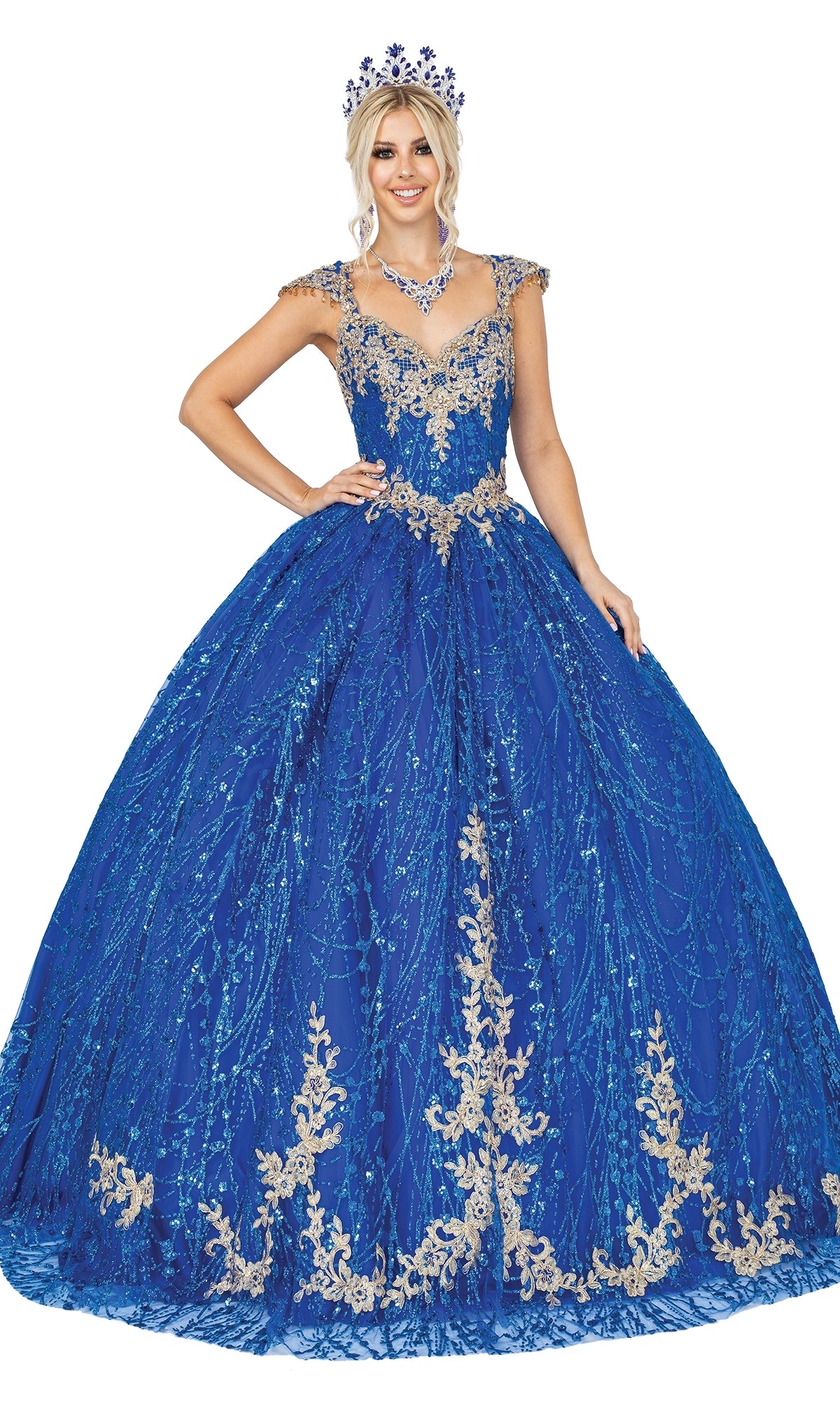 A woman models the Quinceanera Dress 1397 by Dancing Queen—a blue ball gown with gold embroidery and a sweetheart neckline—paired with a matching crown and necklace, smiling against a white background.