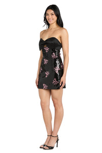 Woman wearing a black strapless short dress with pink bow sequin embellishments on a white background