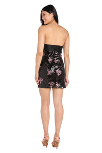 Woman modeling the back of a short black sequin dress with pink bow sequin designs in front of a white background