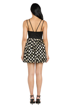 A woman stands facing away, wearing the Morgan 14038 Black and Gold Bubble Party Dress with black heeled sandals for a chic semi-formal look.