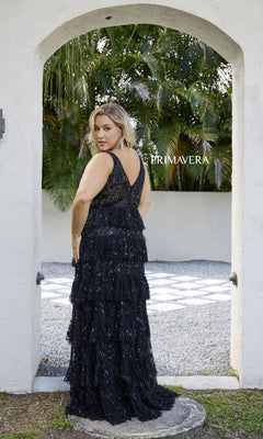 A woman models the Primavera 14073, a long plus-size black prom dress with sequin embellishments, standing outdoors under an archway and looking over her shoulder. The word "PRIMAVERA" appears on the image.