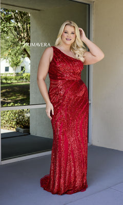 A woman poses outdoors near a window and beige wall, wearing the Plus-Size Long Sequin Prom Dress: Primavera 14075, with greenery in the background.