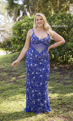 A woman poses outdoors against lush greenery in the Primavera 14079 plus-size long sequin prom gown—a sleeveless, floor-length blue dress with silver starburst sequins on the bodice.