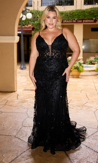 A woman in the Primavera 14106 long plus-size black prom dress stands on a stone patio under an archway, surrounded by plants and building decor.