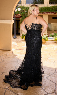 A woman stands outdoors in the Primavera 14106—a long, black, plus-size prom dress with a lace-up back and sequin details—posing confidently with one hand on her hip.