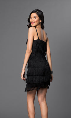 A woman stands and smiles in the Cheryl Creations 1415 Short Fringe Party Dress, a sleeveless, semi-formal design featuring tiered black layers, set against a plain gray background.