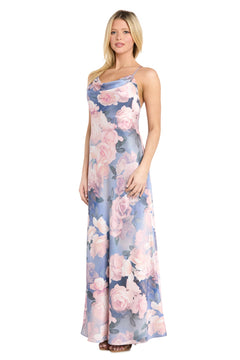 A woman is standing and facing forward, wearing the Morgan 14249 Floral Maxi Slip Dress, which features an elegant cowl neckline and a pink and purple floral pattern on a light blue background.