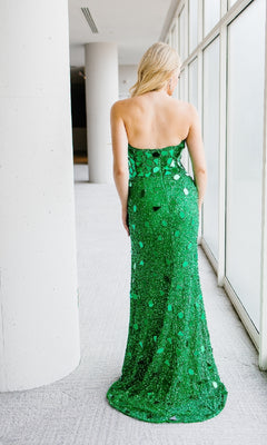 A woman with long blonde hair stands indoors facing away, wearing the Aleta 1429 long prom dress—a strapless, floor-length green sequin gown with a sweetheart neckline that sparkles elegantly.