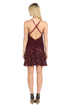 A woman stands facing away, wearing the Short Sequin Hoco Dress: Morgan 14337—a sleeveless burgundy sparkly dress with crisscross back straps—paired with black high-heeled shoes.