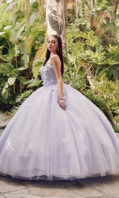 A young woman stands outdoors before lush greenery, wearing the Juliet 1435 Strapless Ball Gown Quinceañera Dress with a full tulle skirt and delicate floral embellishments on the bodice.