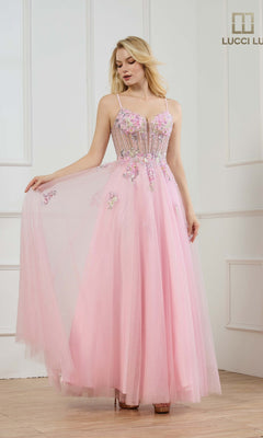 A woman stands in a white-paneled room wearing the Lucci Lu 1437 long pink prom dress, featuring floral embroidery, a sheer bodice, and spaghetti straps.