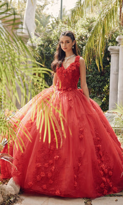 A young woman stands outdoors in the Juliet 1437R Red Ball Gown Quinceañera Dress, featuring floral embellishments and beaded embroidery. She wears a diamond necklace, surrounded by lush greenery.