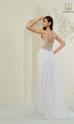 Woman wears the Lucci Lu 1441 long prom dress: a white, floor-length sparkly gown with thin straps, sheer panels, low back, and sleek corset bodice silhouette, standing in a minimalist room with a light background.