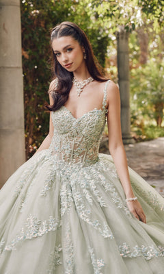 A woman stands outdoors in the Quinceanera Dress By Juliet JT1450J, a light green ball gown with a sweetheart neckline and floral-embroidered tulle, accessorized with a necklace and bracelet.