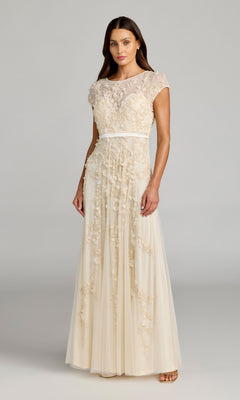 A woman wears the Mac Duggal 14521 Cap-Sleeve Long Formal Dress in cream with floral embroidery and a ribbon belt, making it ideal for special occasions, set against a simple gray background.