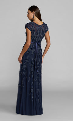 A woman faces away, wearing the Mac Duggal 14521—a floor-length, navy blue cap-sleeve formal dress featuring floral embroidery and a waist ribbon.