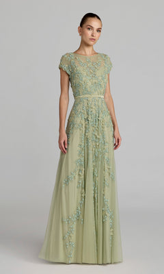 A woman wears the Cap-Sleeve Long Formal Dress: Mac Duggal 14521, a light green, floor-length gown with short sleeves and blue floral embroidery, standing against a plain gray background.