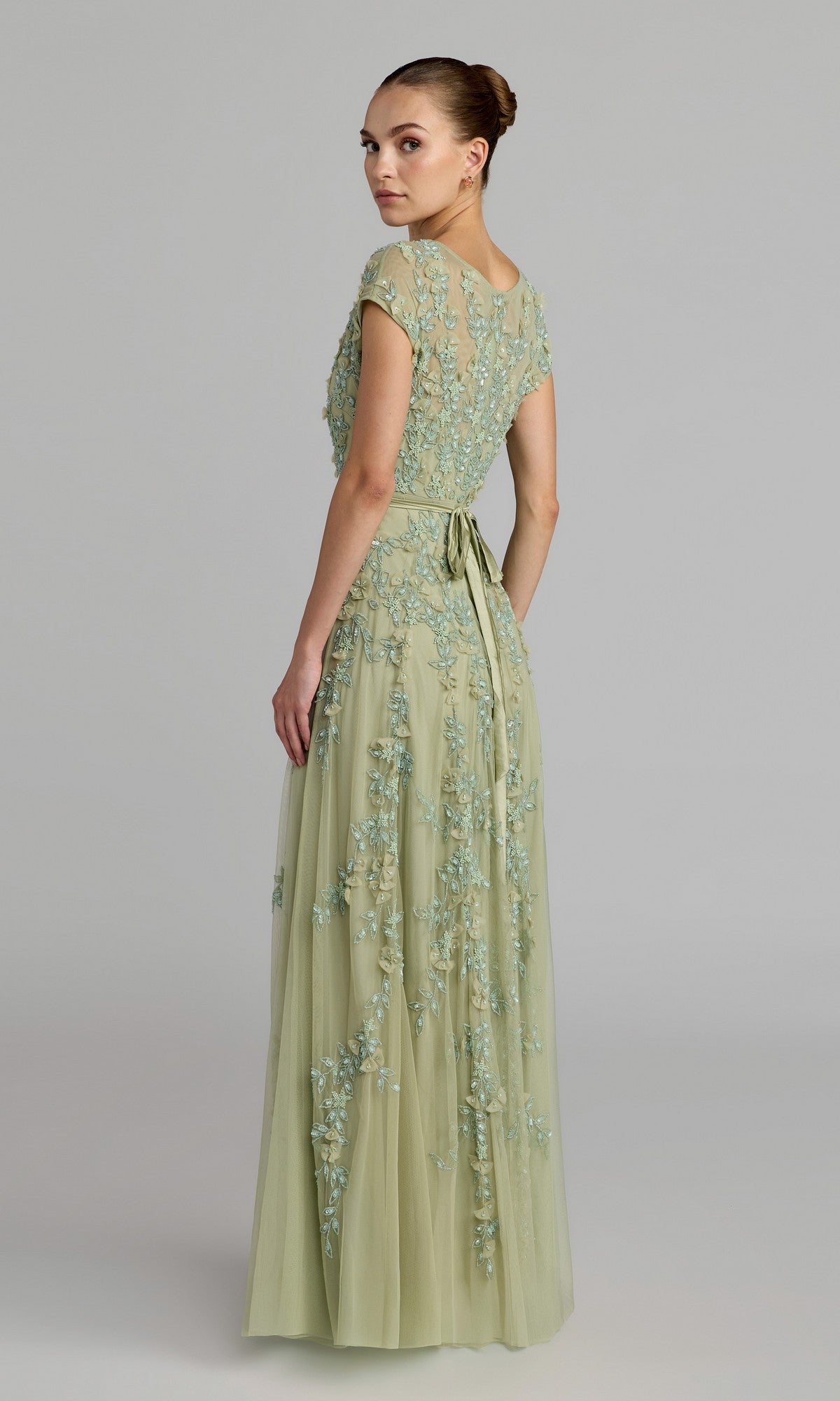 Woman wearing the Cap-Sleeve Long Formal Dress: Mac Duggal 14521 in light green, featuring a sheer embroidered overlay and cap sleeves, standing and looking over her shoulder.