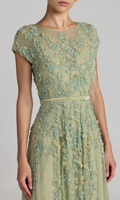 Woman wears the Mac Duggal 14521 Cap-Sleeve Long Formal Dress in light green, featuring intricate floral embroidery and a sheer neckline—ideal for special occasions.