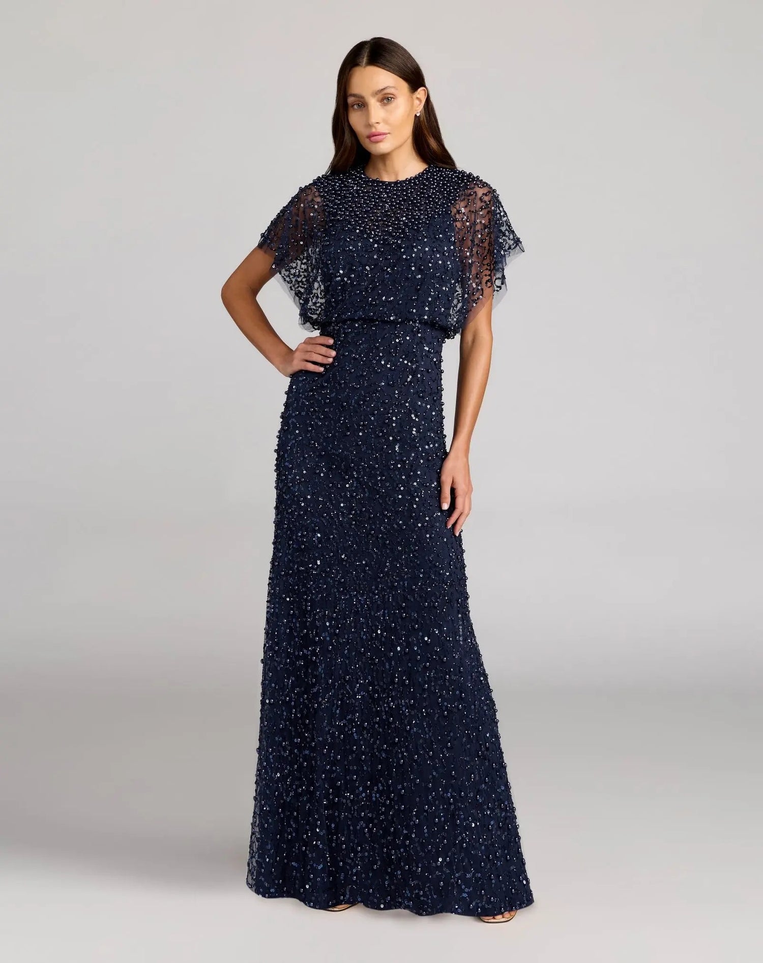 A woman stands wearing the Mac Duggal 14523 Beaded Long Nude Evening Gown against a plain background.