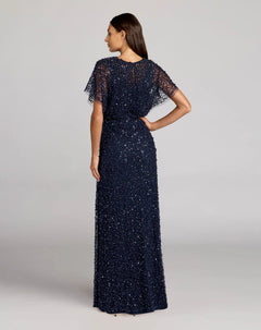 A woman faces away, wearing the Mac Duggal 14523 Beaded Long Nude Evening Gown with sheer short sleeves against a plain background.
