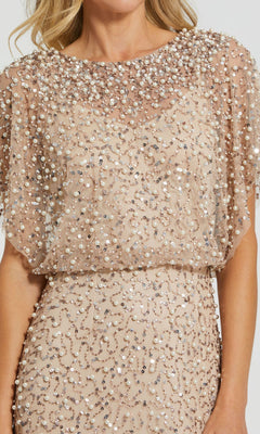 A woman wearing the Mac Duggal 14523 Beaded Long Nude Evening Gown, featuring short sleeves, sequins and beads, and a sheer embellished overlay.